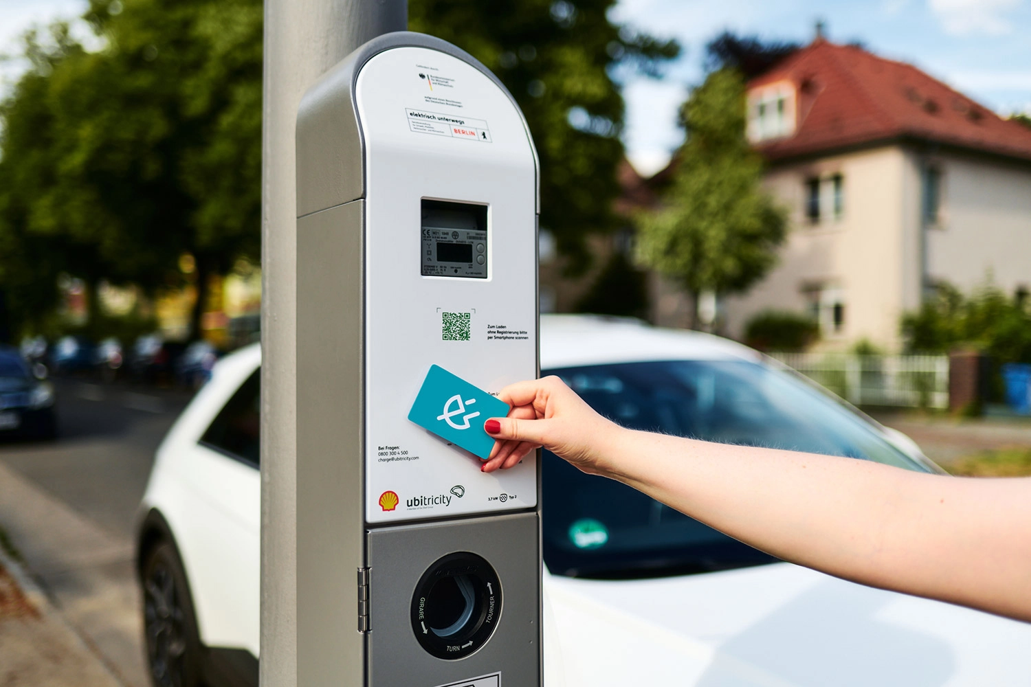 Fahrerin hält RFID-Ladekarte von Shell Recharge an einen öffentlichen AC-Laternenladepunkt von ubitricity in Berlin.
