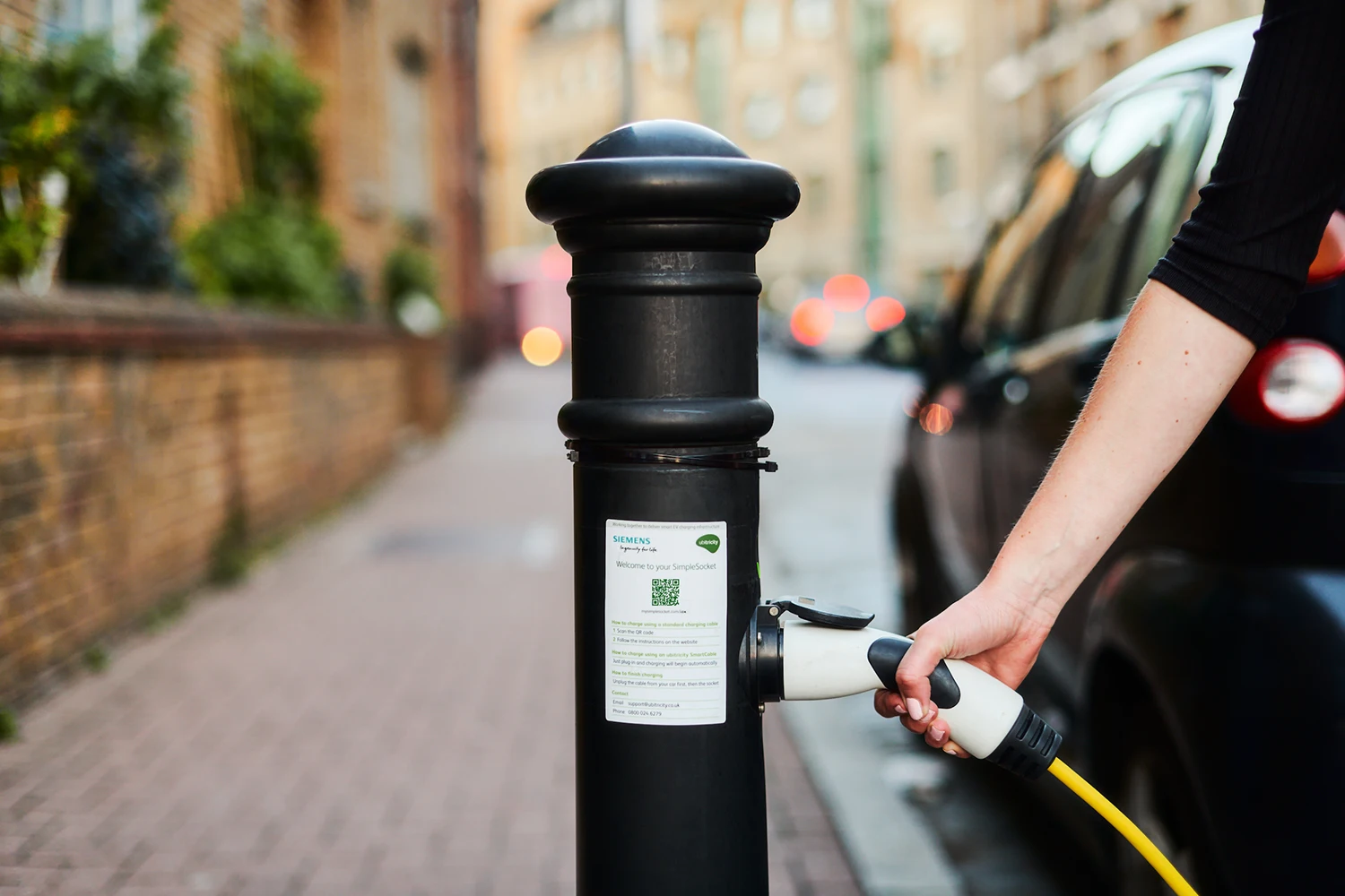 An EV driver is plugging in her electric car to an ubitricity EV bollard charge point in Tower Hamlets, London.
