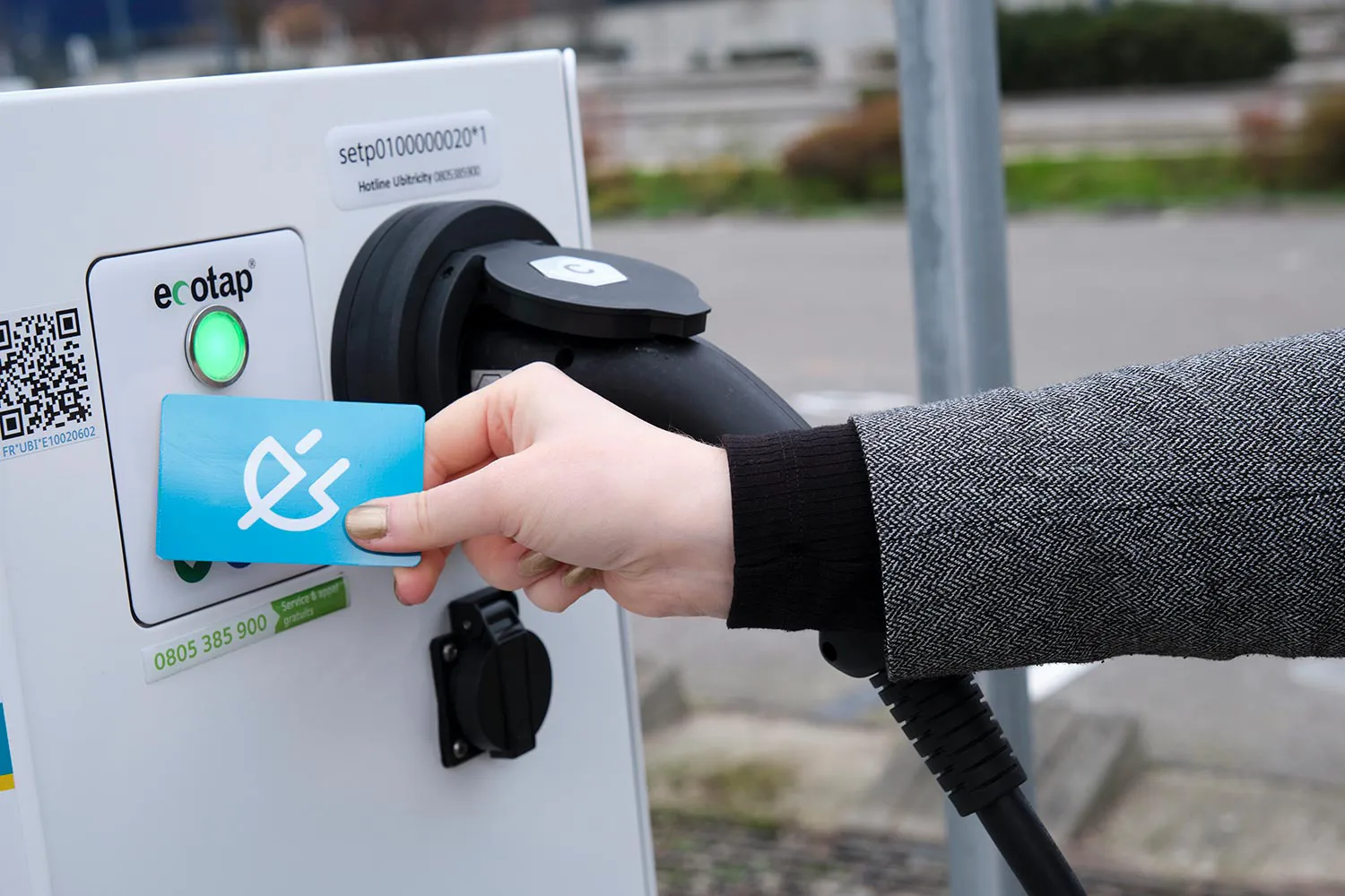 Une femme présente une carte de recharge RFID à une borne de recharge publique de Shell Recharge / ubitricity pour recharger sa voiture électrique.