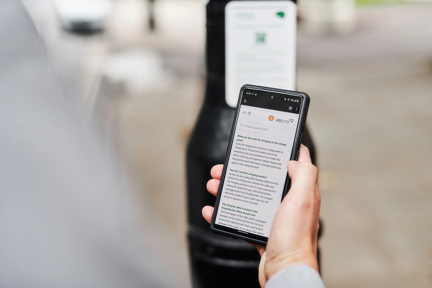 Fahrer mit Smartphone scrollt durch die FAQs für das Aufladen im öffentlichen Raum an einer ubitricity-Ladestation