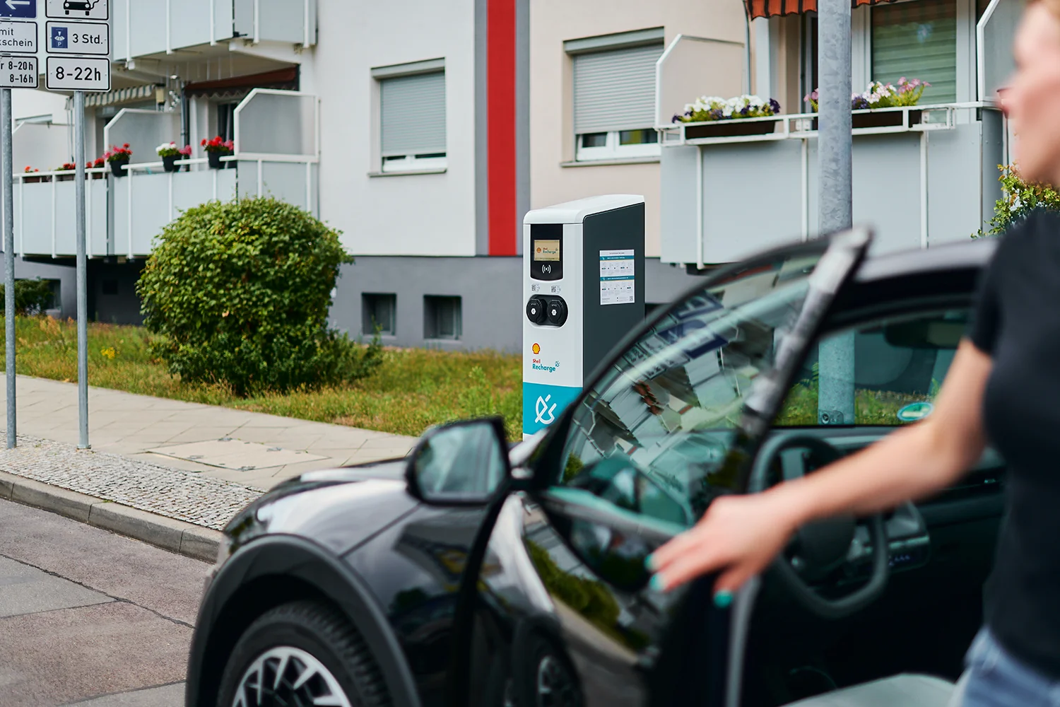 An EV driver is leaving her vehicle to charge at a public Shell Recharge fast charging station using pay-as-you-go, rfid or an emobility app.