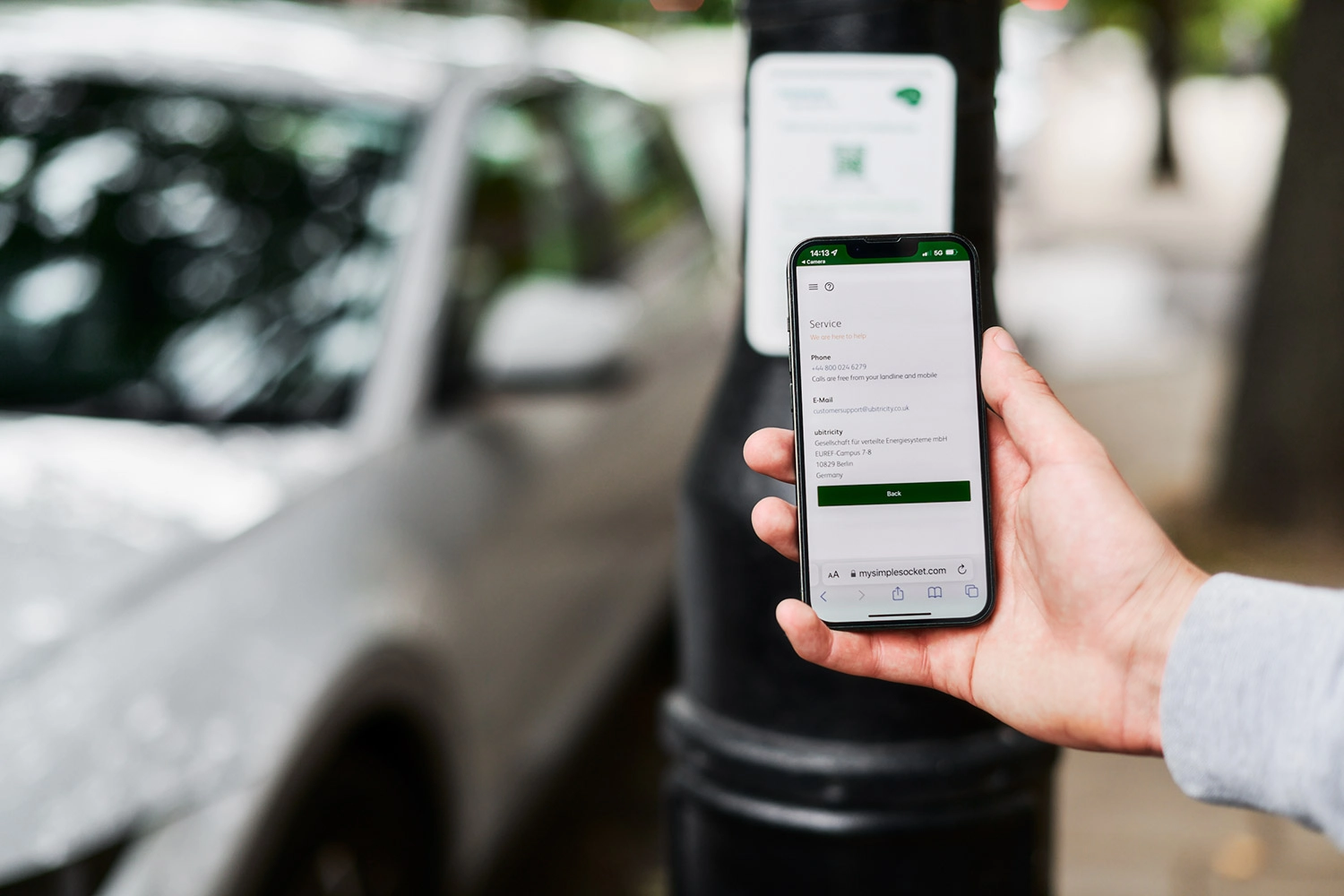 An EV driver is looking at the customer support and contact details of ubitricity, while standing at one of the company's public charging station in London, UK.