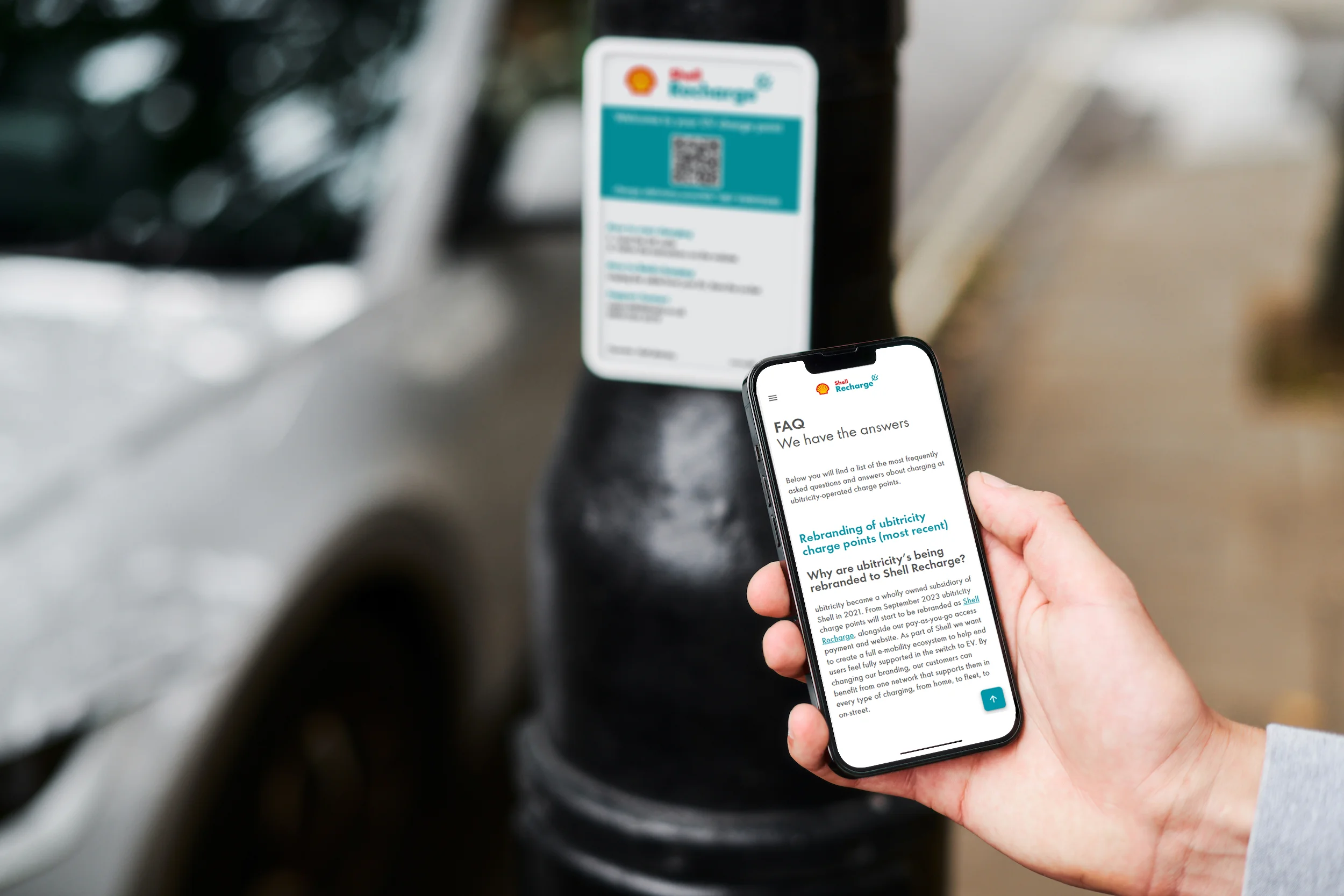 An EV driver is using his smartphone to read ubitricity's FAQs for charging at public on-street Shell Recharge charging stations.