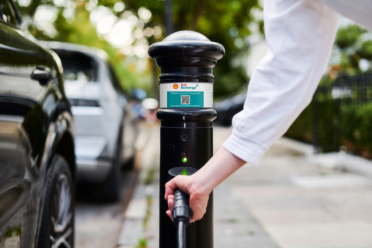 An EV driver is connecting a charging cable to an ubitricity-operated Shell Recharge charging station in the UK.